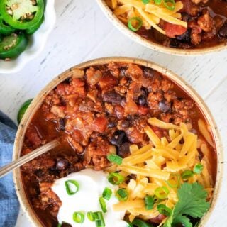 A bowl of turkey chili topped with shredded cheese and sour cream.