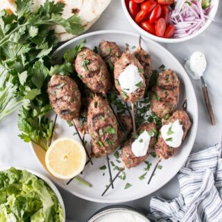 A pile of turkey koftas on a plate with lemon and tzatziki.
