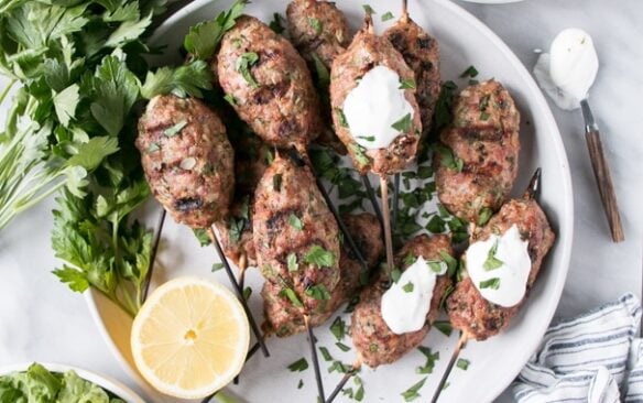 A pile of turkey koftas on a plate with lemon and tzatziki.