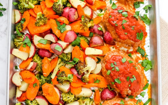 Baked mini turkey meatloaf on a baking sheet with vegetables.