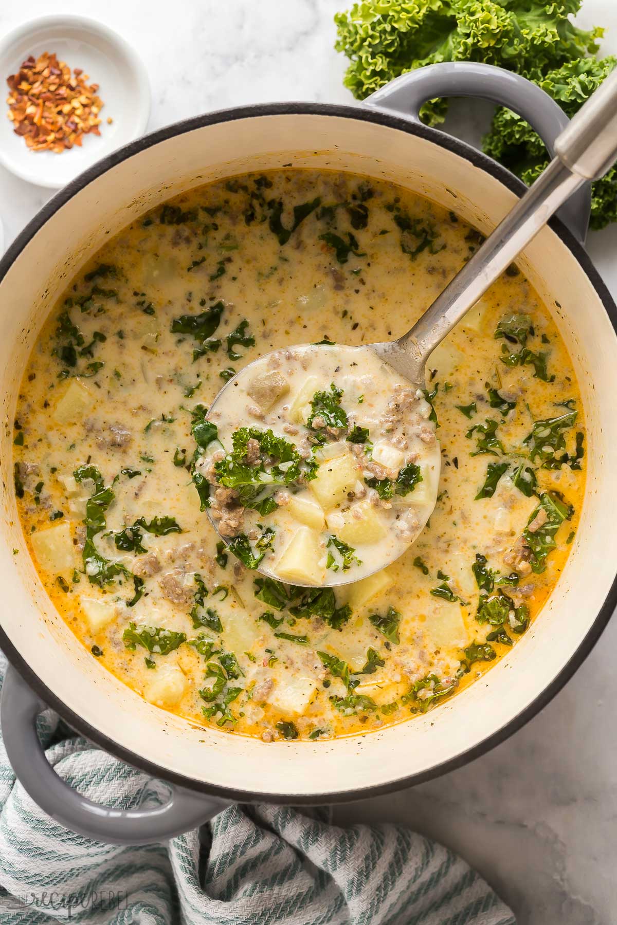 This Zuppa Toscana is the perfect hearty dinner that's ready in just 30 minutes! It's packed with Italian sausage, potatoes and kale, and parmesan cheese! Serve this soup with your favorite crusty bread or a slice of homemade garlic bread! overhead image of metal ladle scooping zuppa toscana from pot