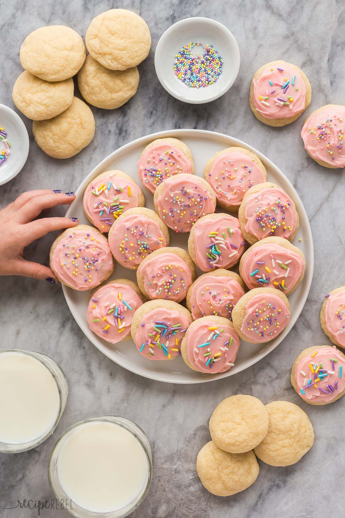 overhead image of frosted and unfrosted sugar cookies with hand reaching to take a cookie