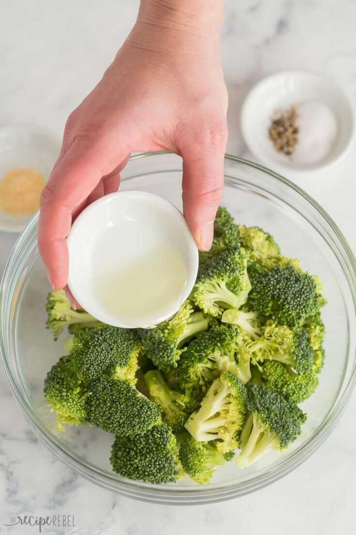 drizzling oil on fresh broccoli florets in bowl