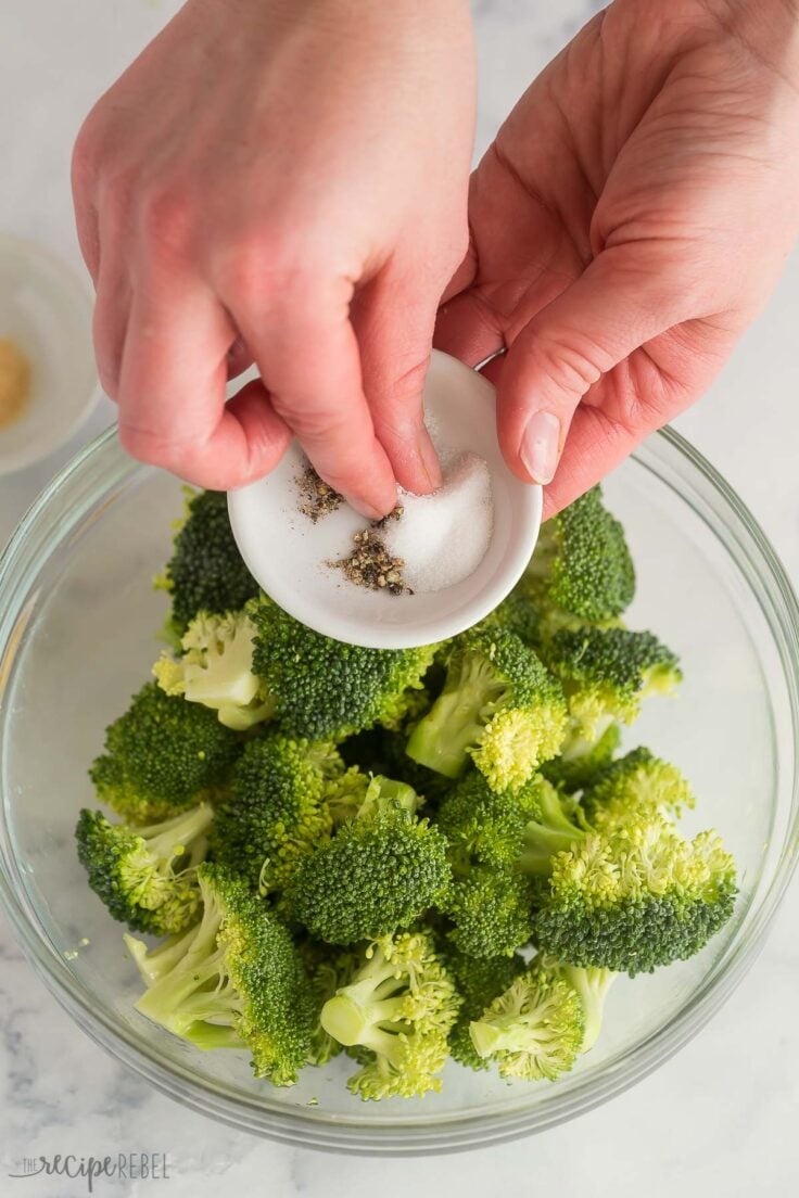 sprinkling salt and pepper on broccoli in glass bowl