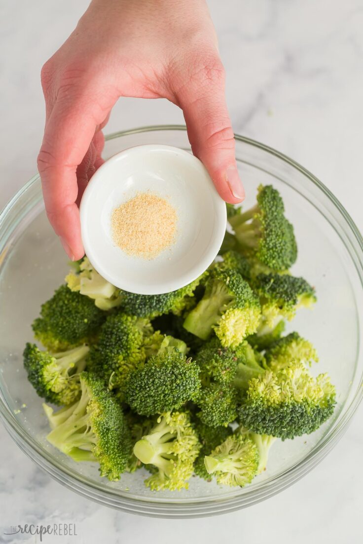 sprinkling garlic powder on fresh broccoli in glass bowl