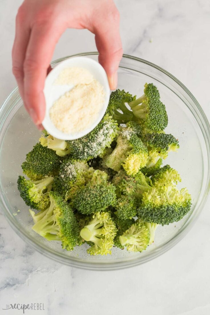 sprinkling parmesan on fresh broccoli in glass bowl