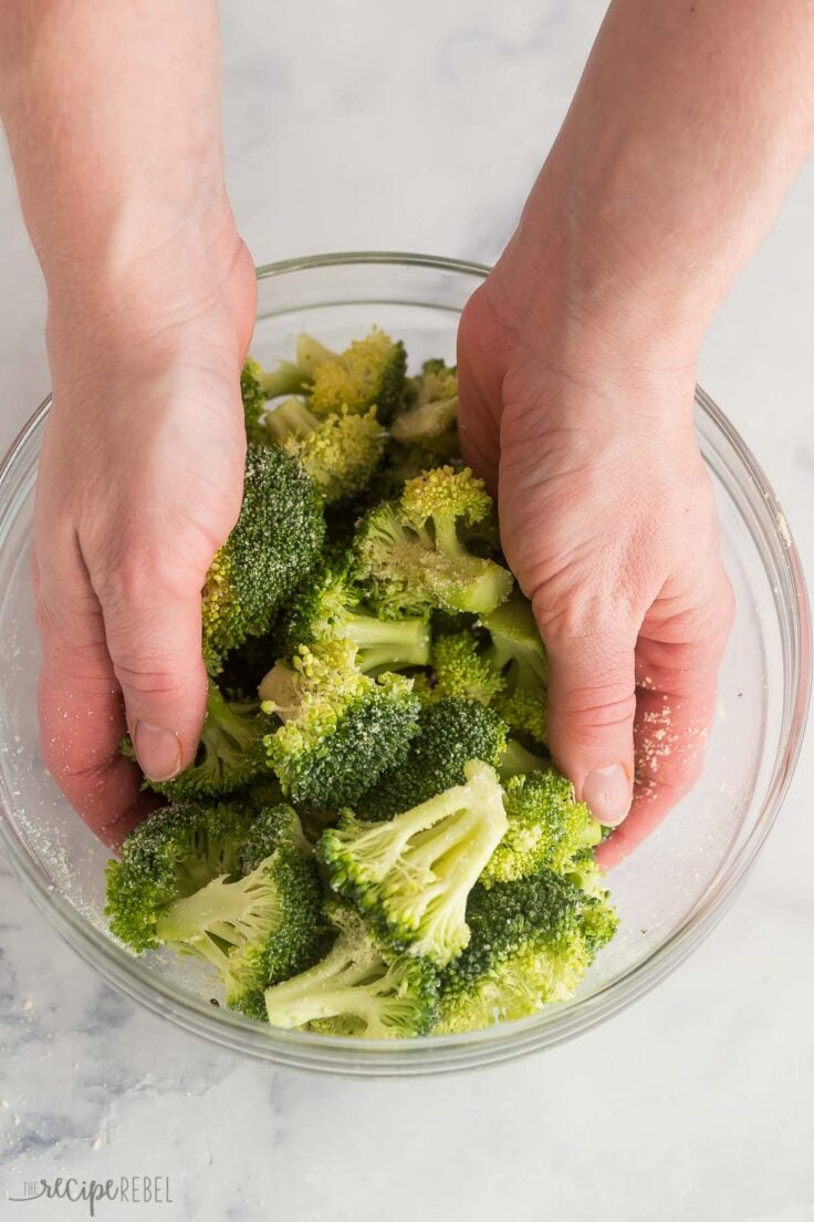 using hands to combine broccoli and seasonings in glass bowl