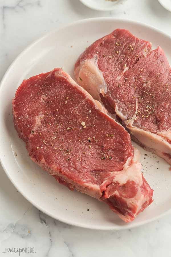 uncooked striploin steaks sprinkled with salt and pepper