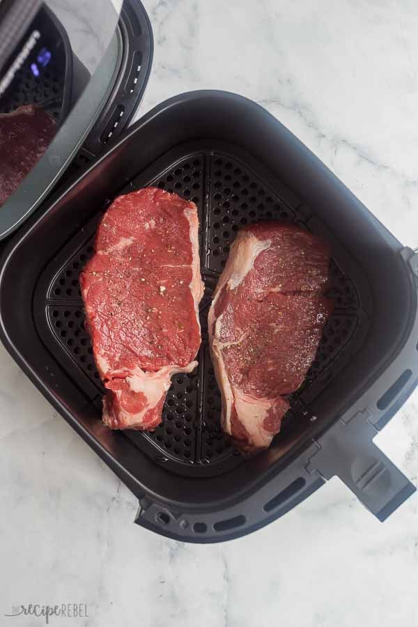 two uncooked steaks in air fryer basket