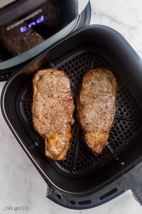 two cooked steaks in air fryer basket