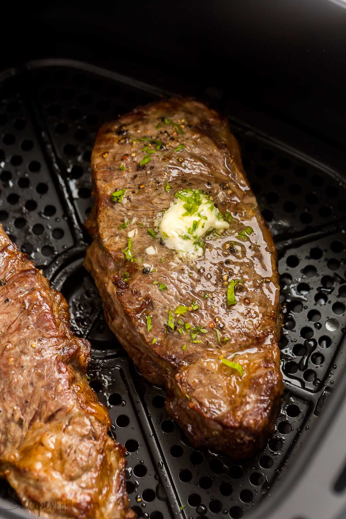 close up image of striploin steak in air fryer with butter and fresh parsley on top