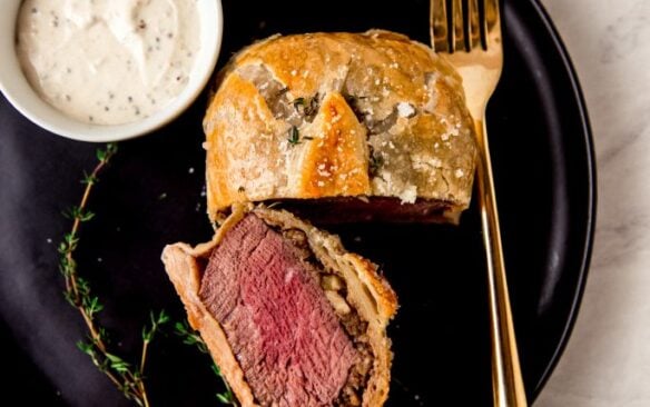 An individual beef wellington on a plate, cut in half to reveal the layers.