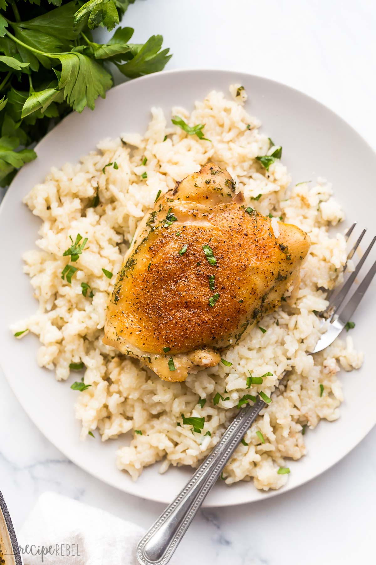 one baked chicken thigh on top of bed of rice on plate with fork