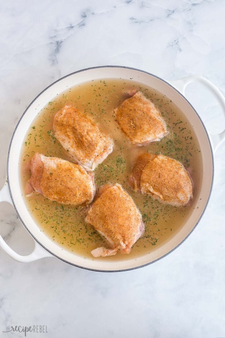 chicken thighs in large white pan on top of rice and liquid