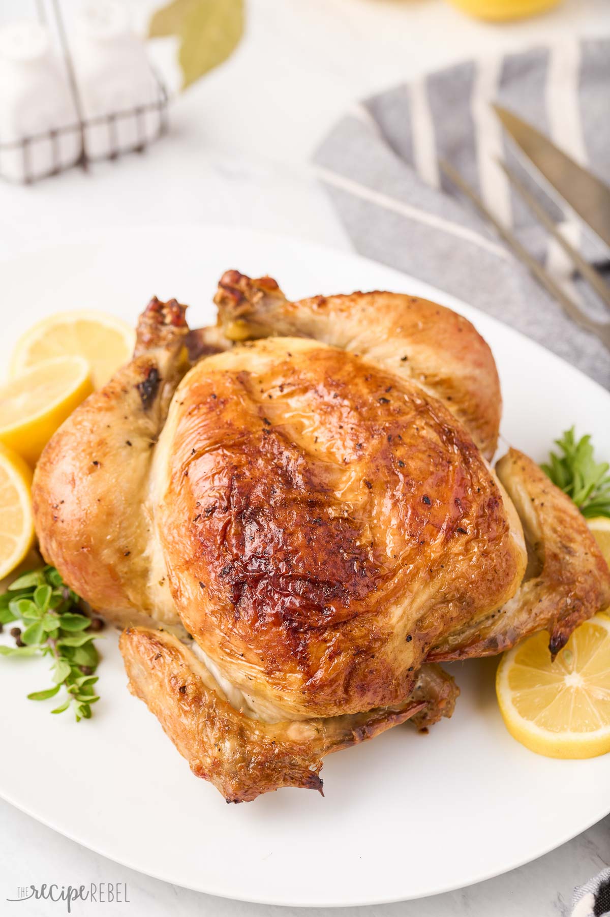 close up image of roast chicken on white plate with lemon and greens