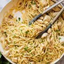 overhead image of chicken carbonara in white skillet with tongs and fresh parsley