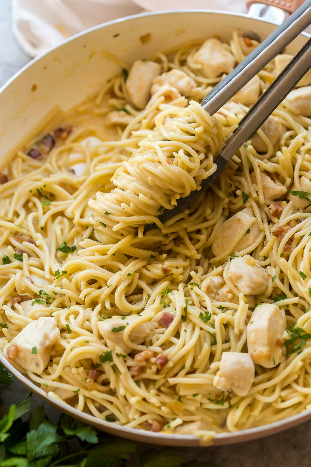 close up image of tongs twirling chicken carbonara