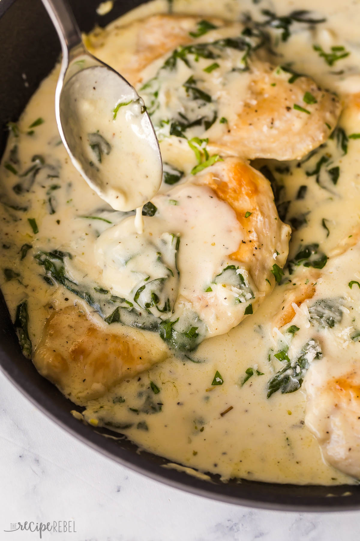 close up image of chicken breast in black skillet with sauce being poured over