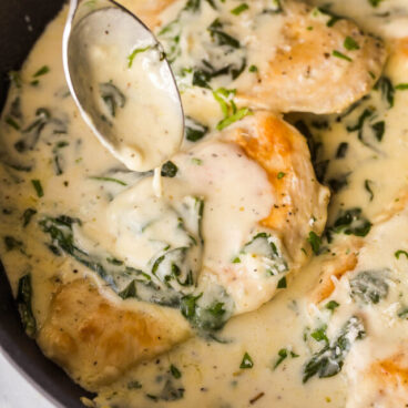 close up image of chicken breast in black skillet with sauce being poured over