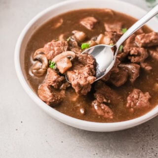 A bowl full of saucy beef tips and gravy with mushrooms.