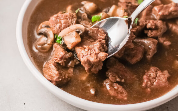 A bowl full of saucy beef tips and gravy with mushrooms.