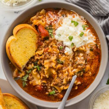 square overhead image of lasagna soup in bowl with cheese and garlic bread