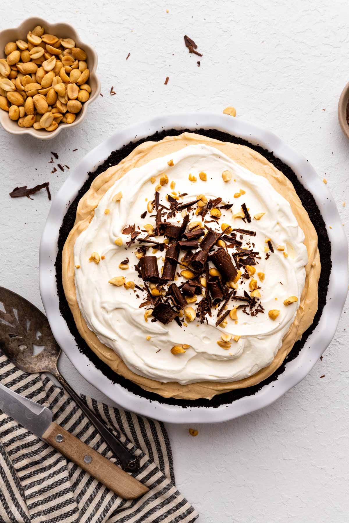 This Peanut Butter Pie is completely no bake and made with a chocolate Oreo crust, peanut butter cream cheese filling, and topped with more chocolate! Step by step recipe video down below. #peanutbutter #pie #nobake #dessert #recipes | peanut butter recipes | easy dessert recipes | no bake dessert overhead image of whole peanut butter pie with whipped cream and chocolate shavings.