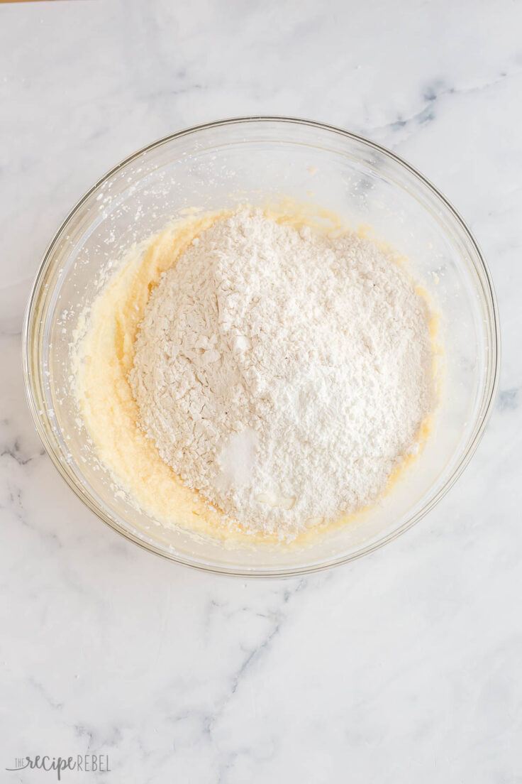 adding flour to sugar cookie dough in glass bowl