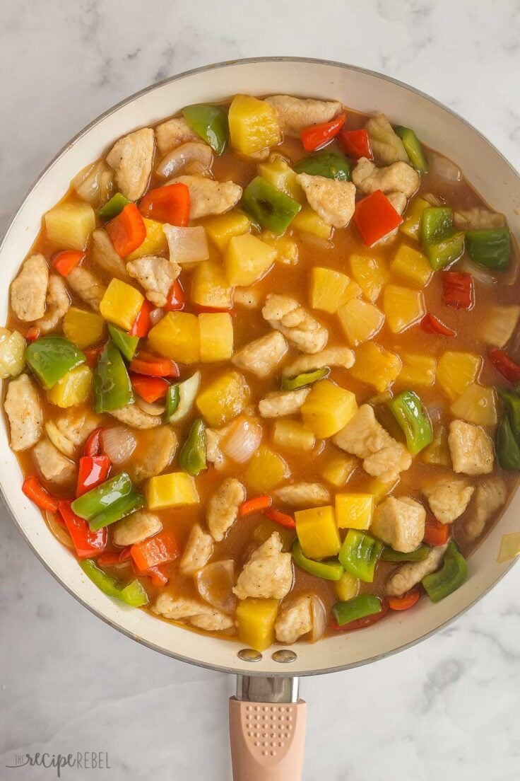 chicken and peppers in skillet with pineapple and sweet and sour sauce added