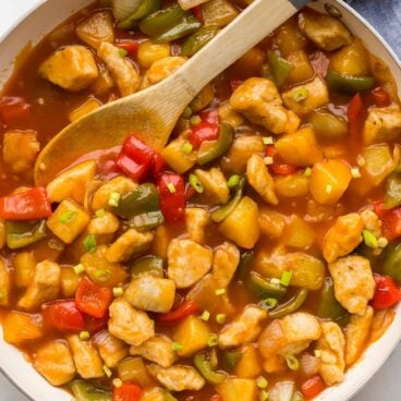 overhead image of sweet and sour chicken in white skillet with wooden spoon
