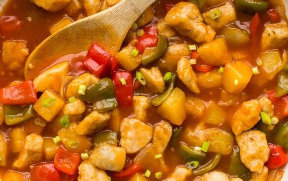 overhead image of sweet and sour chicken in white skillet with wooden spoon