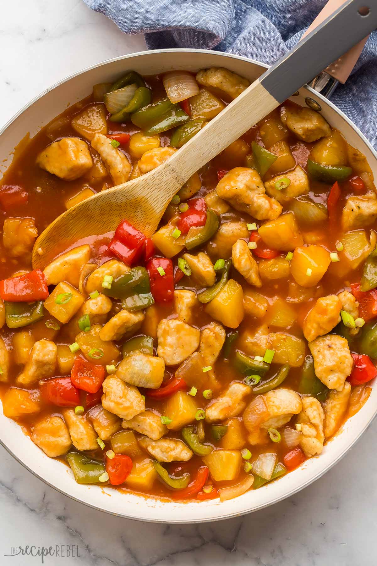 overhead image of sweet and sour chicken in white skillet with wooden spoon