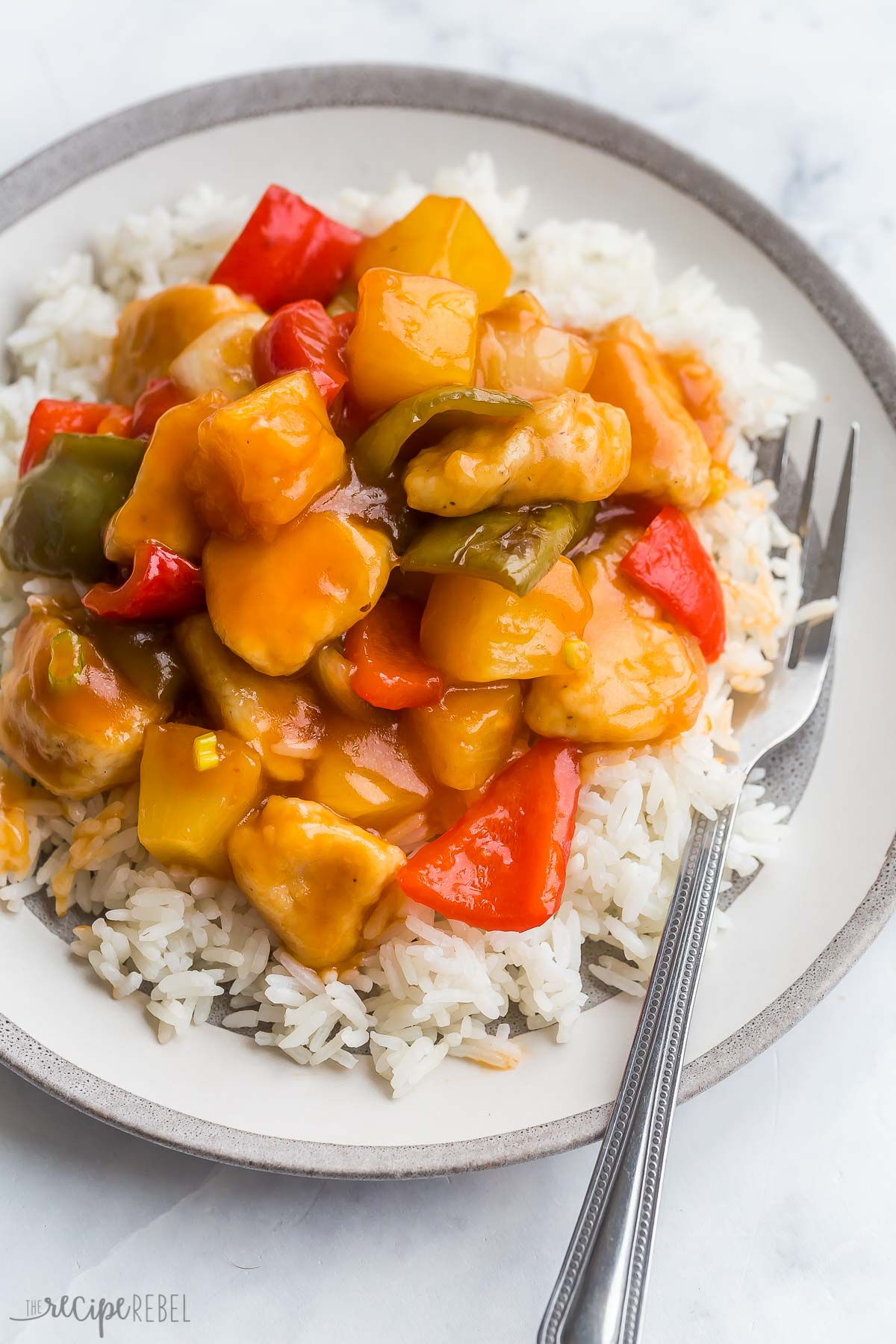 close up image of sweet sour chicken on white plate with rice