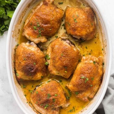 overhead image of baked chicken thighs in white baking dish with fresh parsley