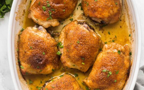 overhead image of baked chicken thighs in white baking dish with fresh parsley