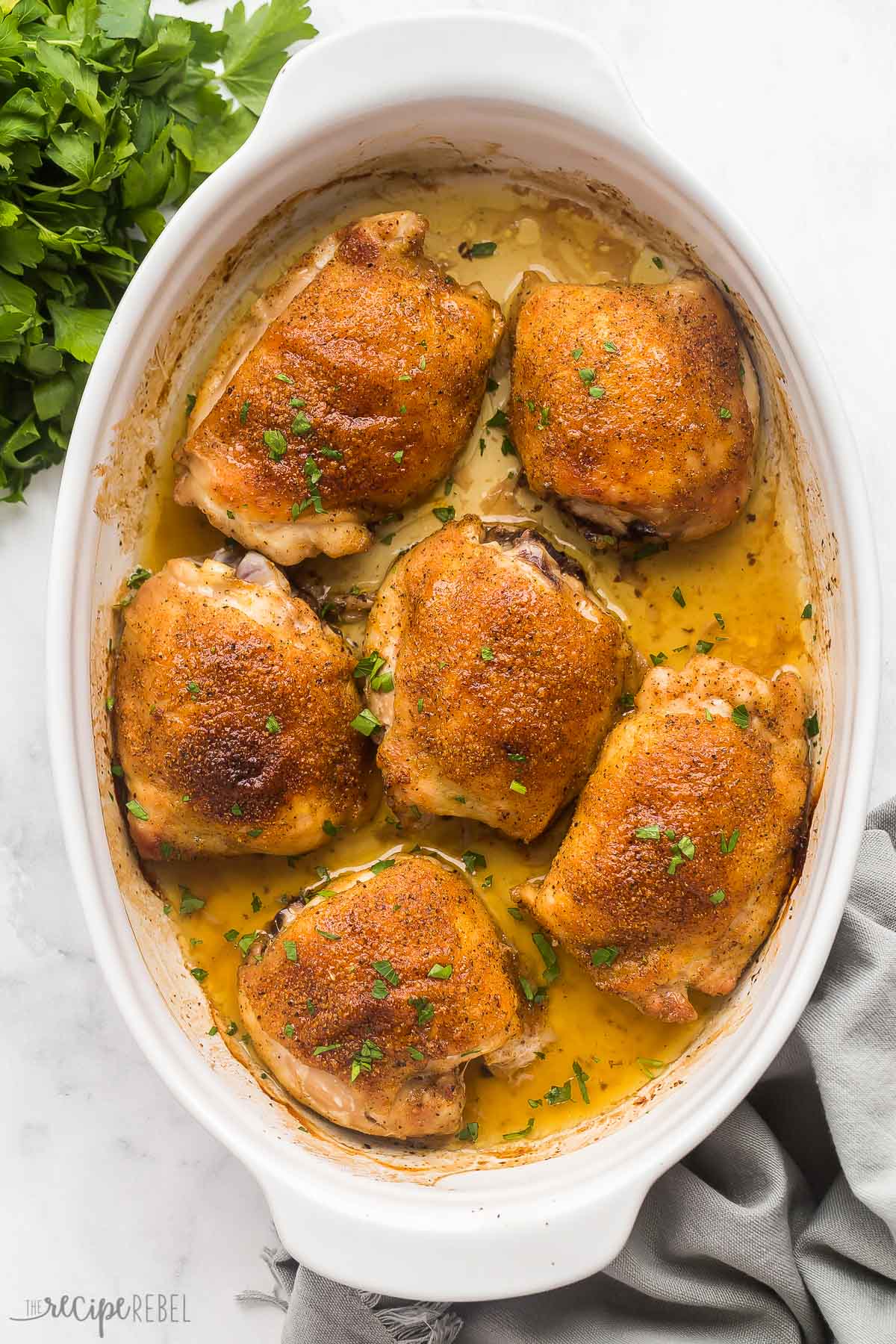 overhead image of baked chicken thighs in white baking dish with fresh parsley