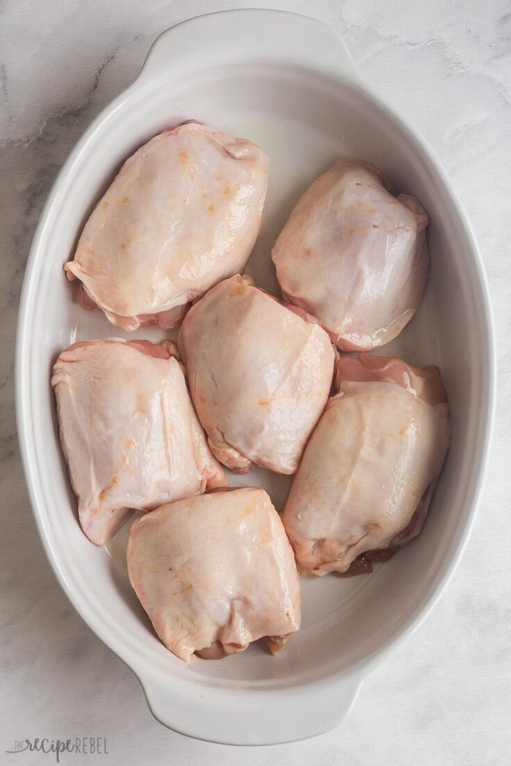 overhead image of bone in skin on chicken thighs in white baking dish