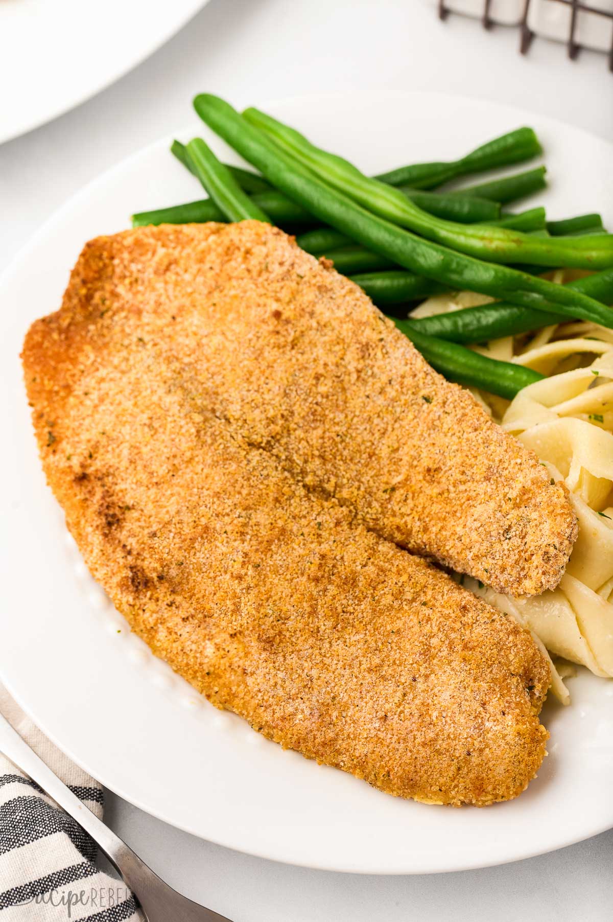 close up image of crispy baked tilapia with green beans and noodles