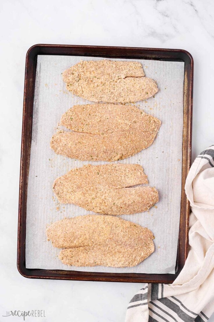 breaded tilapia filets on baking sheet ready to bake