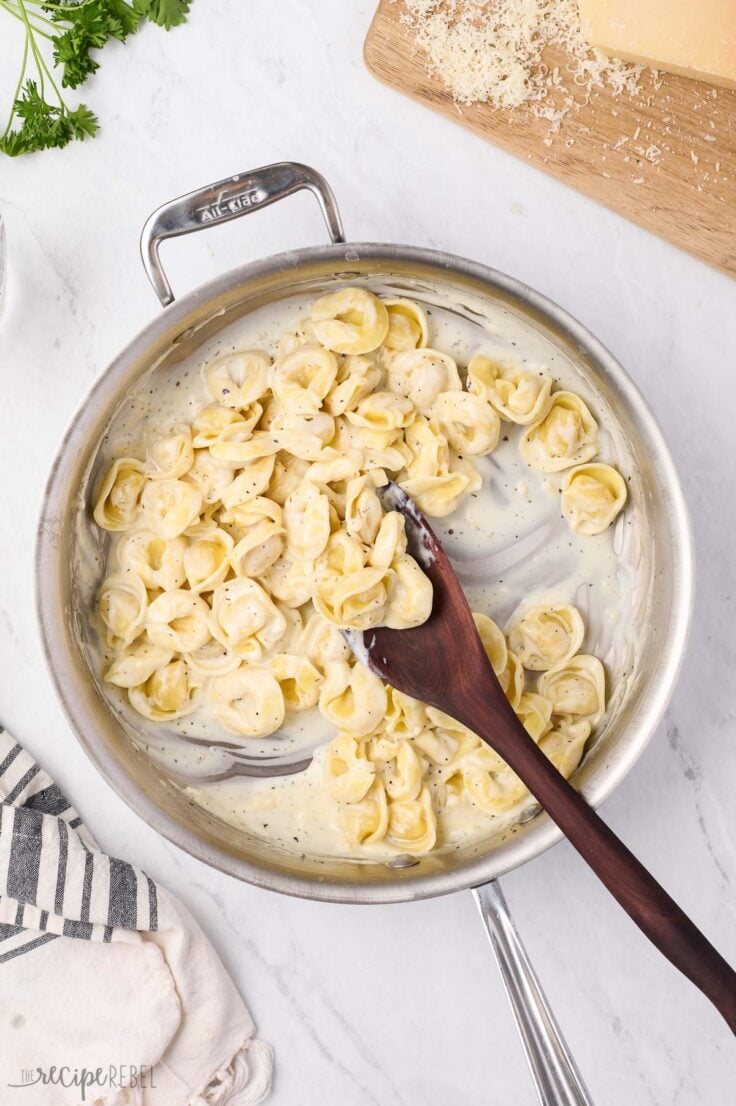 cooked tortellini added to sauce in stainless steel pan