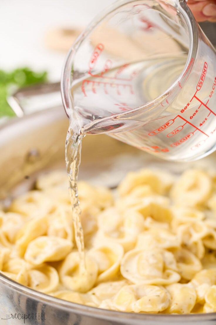 pasta water being added to creamy tortellini in pan