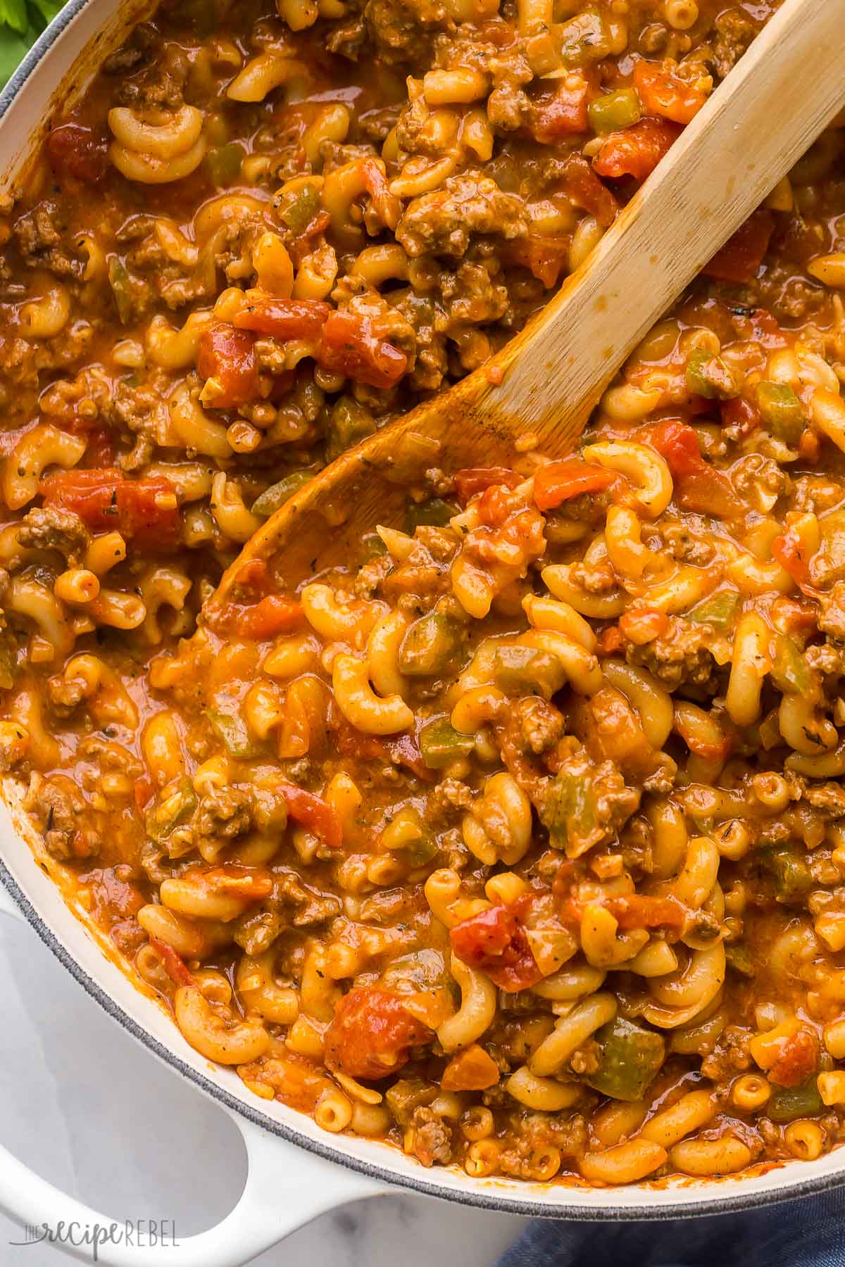 This American Goulash recipe is a classic dinner that's ready in just 30 minutes! It's made up of macaroni noodles, tender ground beef, and veggies simmered in a rich and flavorful tomato-based sauce. #pasta #recipe | dinner ideas | easy dinner | macaroni | pasta recipe | easy pasta | healthy dinner close up image of goulash in pan with wooden spoon