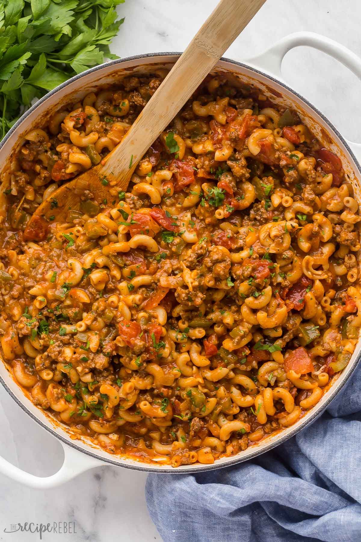 This American Goulash recipe is a classic dinner that's ready in just 30 minutes! It's made up of macaroni noodles, tender ground beef, and veggies simmered in a rich and flavorful tomato-based sauce. #pasta #recipe | dinner ideas | easy dinner | macaroni | pasta recipe | easy pasta | healthy dinner overhead image of goulash with wooden spoon stuck in