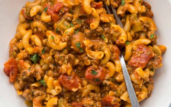 overhead image of american goulash recipe in white bowl with fork