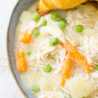 A bowl of creamy chicken pot pie served with a flaky croissant.