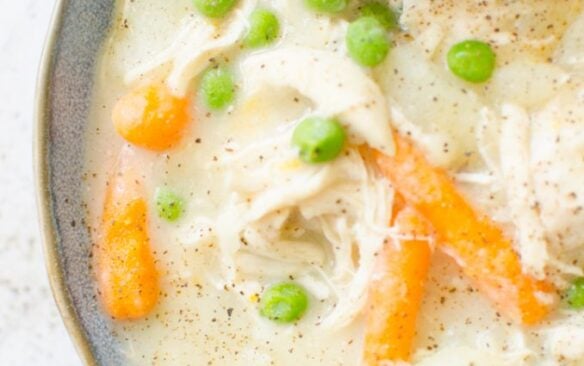 A bowl of creamy chicken pot pie served with a flaky croissant.