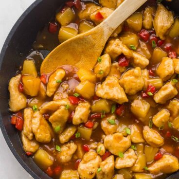 overhead image of pineapple chicken in black skillet with wooden spoon