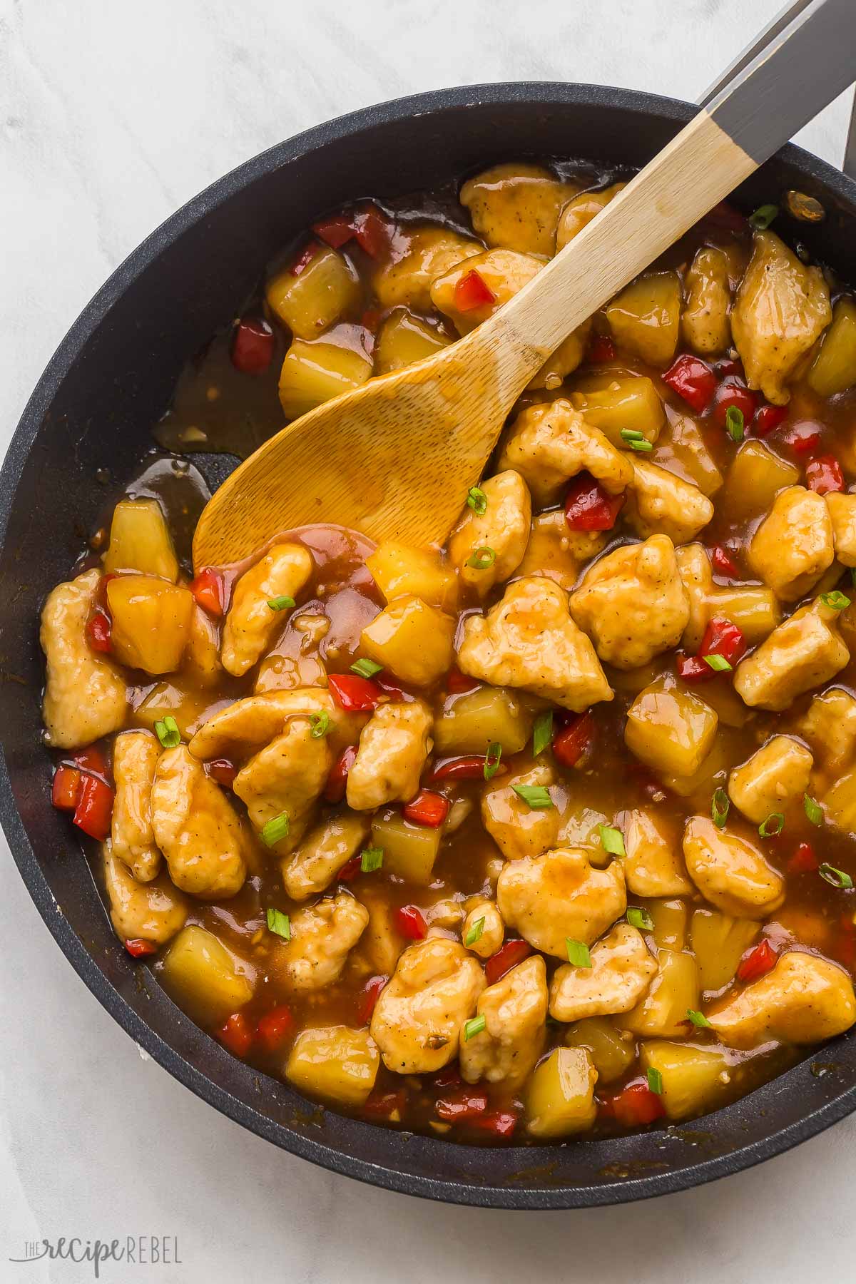 overhead image of pineapple chicken in black skillet with wooden spoon