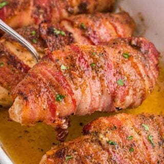 A serving spoon scoops up a baked chicken breast wrapped in bacon.