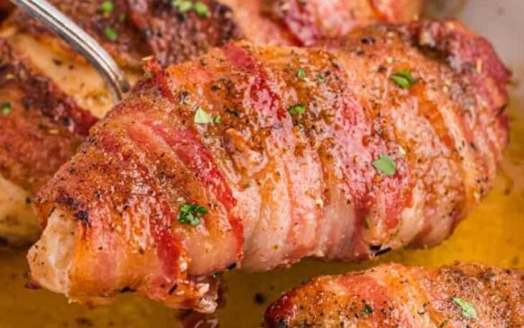 A serving spoon scoops up a baked chicken breast wrapped in bacon.